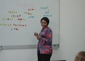 A female teacher explaining an English lesson to students in a classroom with a whiteboard.
